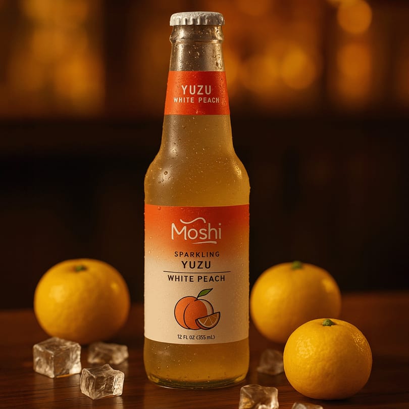 A chilled bottle of Moshi Sparkling Yuzu White Peach drink, surrounded by yuzu fruits and ice cubes.