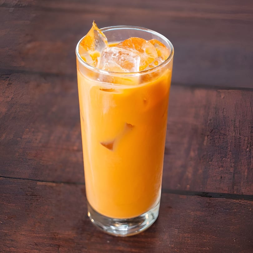 A tall glass of iced Thai tea with a rich orange color sits on a dark wooden table.