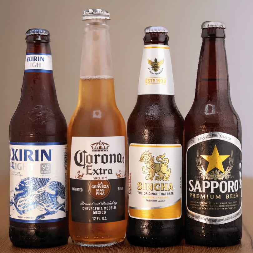 Four cold beer bottles, including Kirin Light, Corona Extra, Singha, and Sapporo Premium Beer.