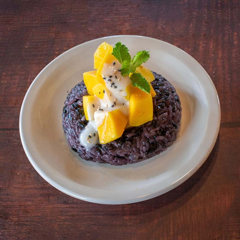 Thai mango sticky rice with black glutinous rice, fresh mango, coconut milk, and mint.